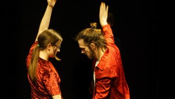 eleanor and lewys wearing red outfits facing towards each other, moving with one arm in the air