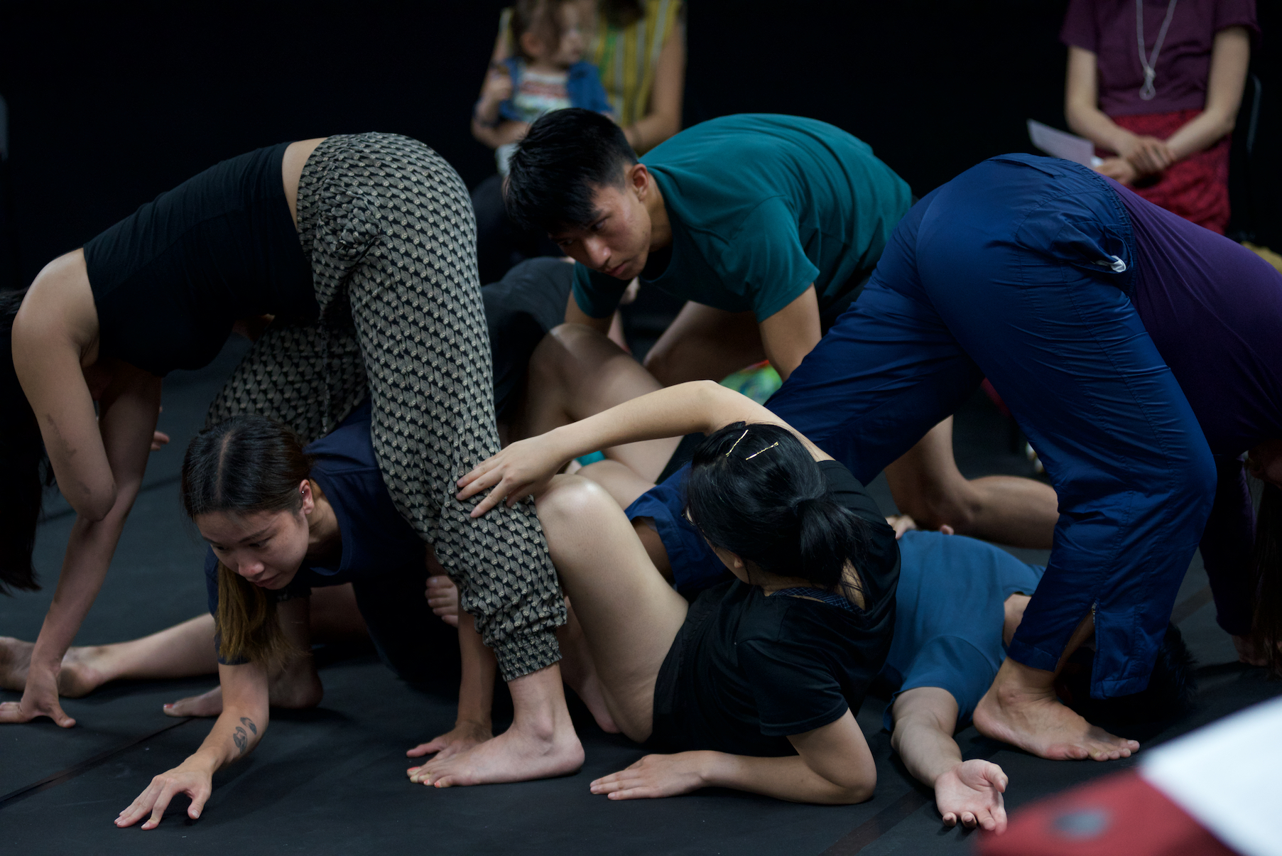 six dancers in dark clothes dancing, wrapping themselves around each other on the floor