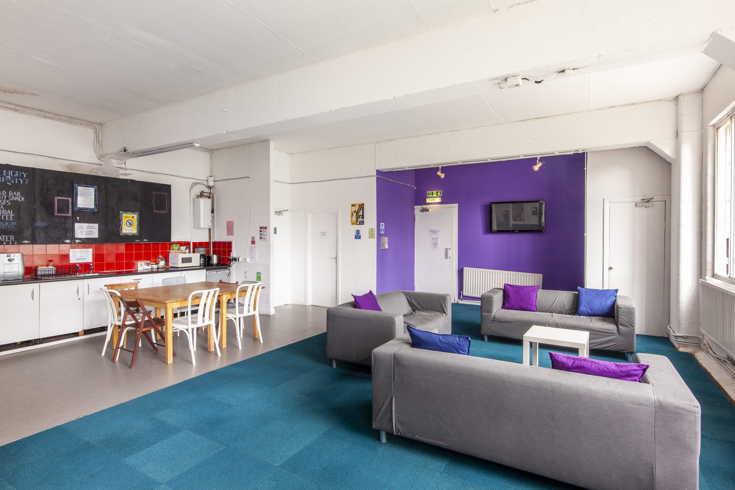 Image of three grey sofas and kitchen area with dining table in Chisenhale Dance Space lounge