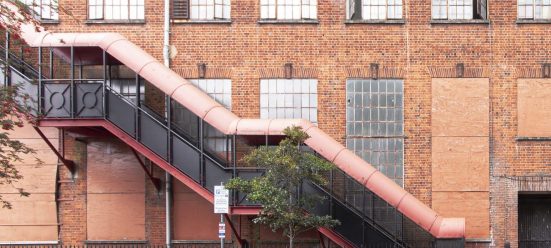 A red brick warehouse building with a red fire escape extending upwards to the left