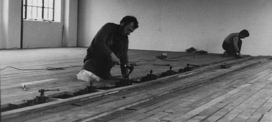 Black and white photo of two men hammering the dance studio floor